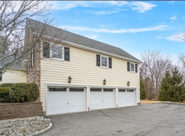 view of property exterior with driveway, an attached garage, and a shingled roof