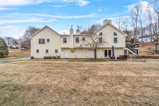 back of property featuring stairs, a lawn, and a chimney