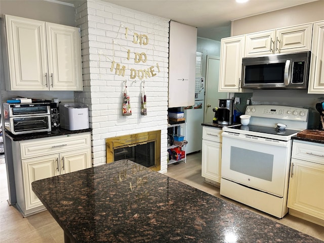 kitchen with a fireplace, light wood finished floors, white electric range, stainless steel microwave, and dark stone countertops