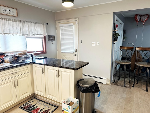 kitchen featuring dark stone counters, light wood-style flooring, ornamental molding, cream cabinetry, and a baseboard heating unit