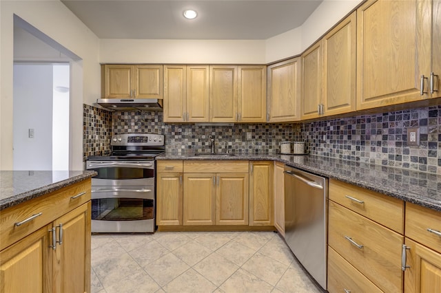 kitchen featuring under cabinet range hood, a sink, appliances with stainless steel finishes, tasteful backsplash, and dark stone countertops