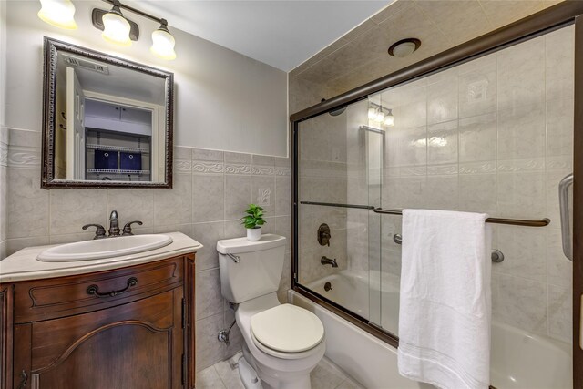 full bath featuring toilet, shower / bath combination with glass door, vanity, and tile walls