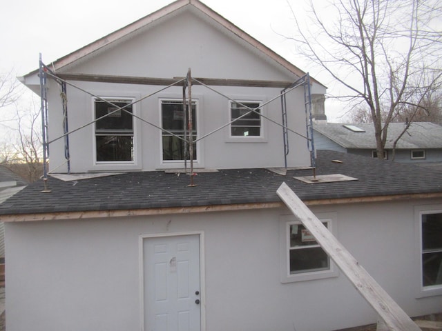 rear view of house featuring a shingled roof and stucco siding