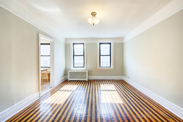 empty room featuring radiator, wood-type flooring, baseboards, and crown molding