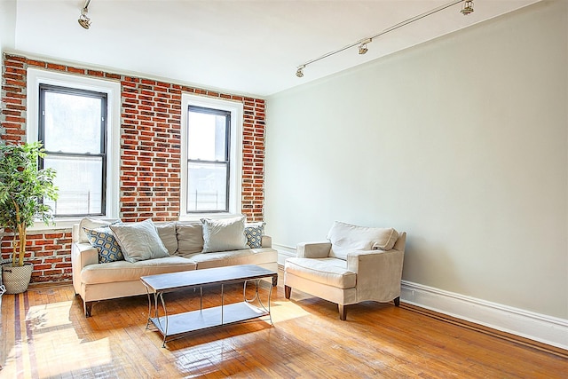 living area with track lighting, wood-type flooring, brick wall, and baseboards