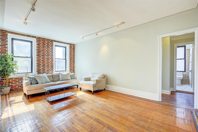 living room with brick wall, rail lighting, and hardwood / wood-style flooring