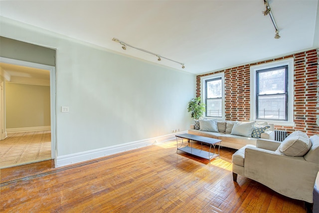 living area featuring track lighting, brick wall, baseboards, and hardwood / wood-style floors