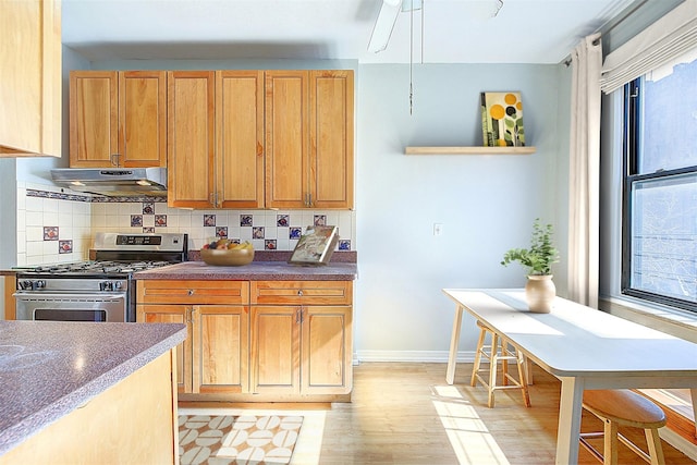 kitchen with stainless steel gas range oven, under cabinet range hood, backsplash, dark countertops, and baseboards