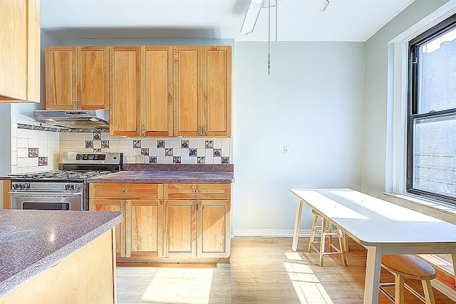 kitchen with stainless steel gas range, extractor fan, dark countertops, light wood-style flooring, and decorative backsplash