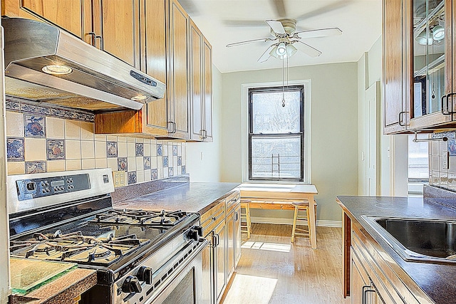 kitchen featuring stainless steel gas stove, under cabinet range hood, light wood-style floors, a ceiling fan, and backsplash