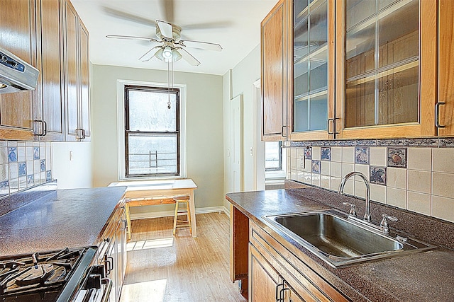 kitchen with a sink, dark countertops, light wood-style floors, gas range, and a ceiling fan