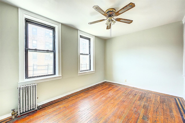 empty room featuring radiator, a ceiling fan, wood-type flooring, and baseboards