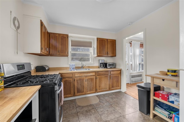 kitchen featuring radiator, stainless steel range with gas stovetop, ornamental molding, brown cabinetry, and a sink