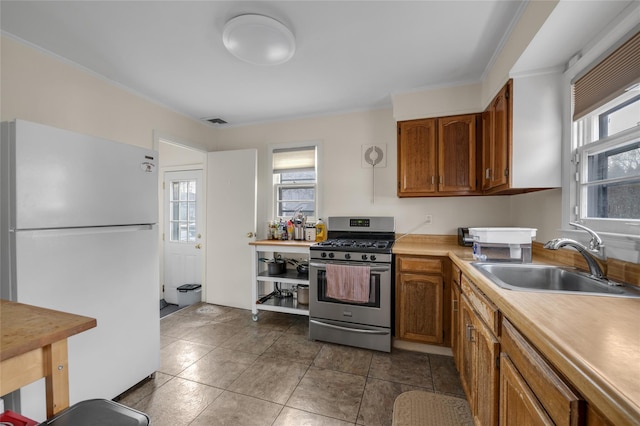 kitchen featuring visible vents, stainless steel range with gas cooktop, brown cabinets, freestanding refrigerator, and a sink