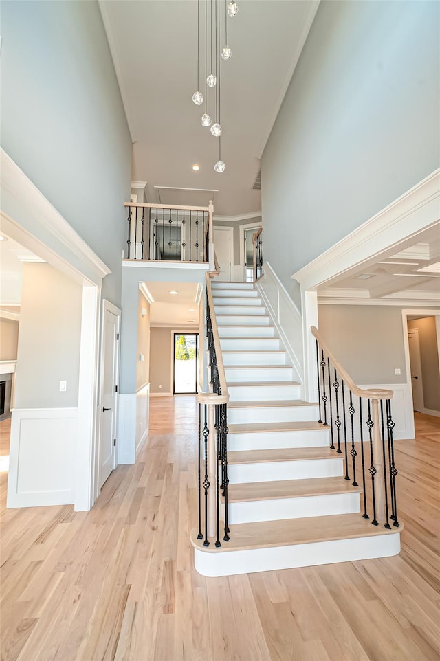 staircase featuring a wainscoted wall, a decorative wall, a towering ceiling, ornamental molding, and wood finished floors