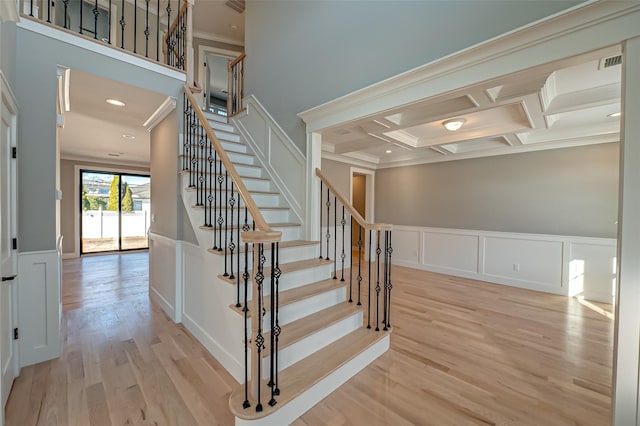 stairway with visible vents, coffered ceiling, ornamental molding, wood finished floors, and a decorative wall