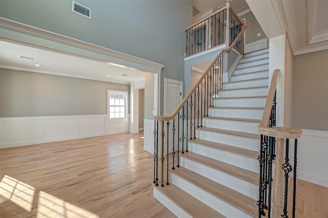 stairway featuring crown molding, visible vents, a decorative wall, wainscoting, and wood finished floors