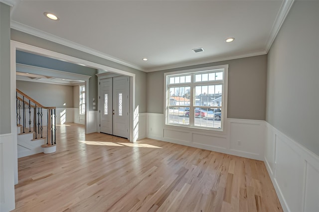 entryway featuring light wood-style floors, a wainscoted wall, a healthy amount of sunlight, and stairs