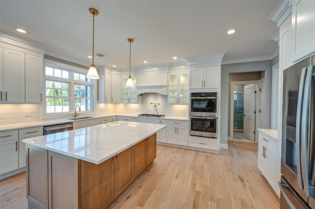 kitchen with stainless steel appliances, a sink, light wood-style floors, decorative backsplash, and crown molding