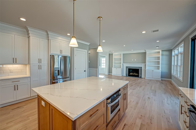 kitchen featuring light stone counters, light wood-style flooring, stainless steel appliances, a center island, and crown molding