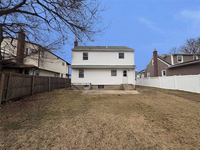 rear view of property featuring a lawn, a fenced backyard, a chimney, and entry steps