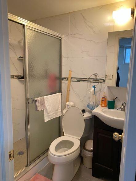 bathroom with tile walls, toilet, a shower stall, and vanity