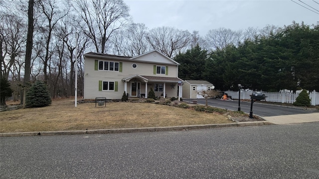 traditional home featuring covered porch, aphalt driveway, a front yard, and fence