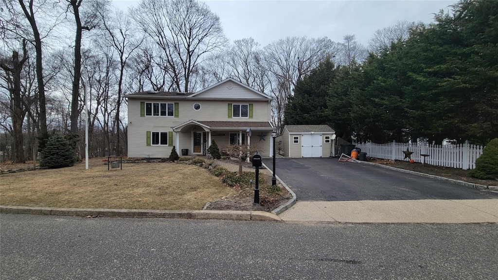 traditional home with aphalt driveway, an outdoor structure, fence, and a storage shed