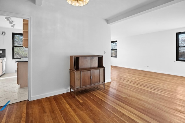 spare room with a wealth of natural light, light wood-type flooring, baseboards, and beam ceiling