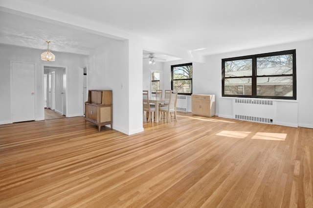 unfurnished living room with radiator, baseboards, and light wood-style floors