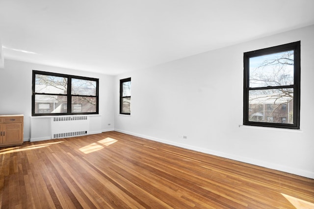 unfurnished room with radiator, wood finished floors, and baseboards