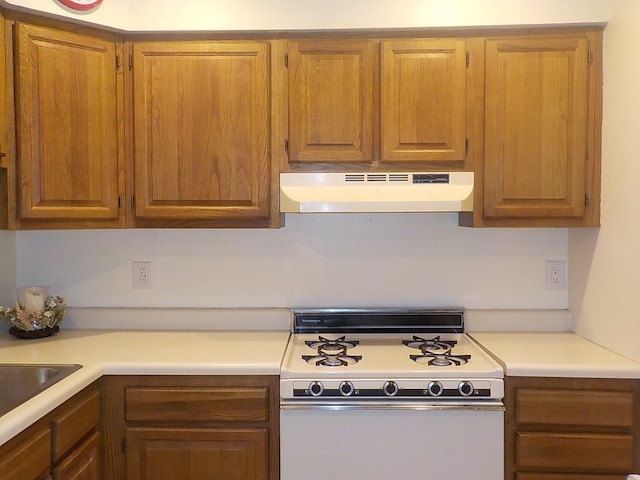 kitchen featuring light countertops, white gas range oven, brown cabinets, and under cabinet range hood