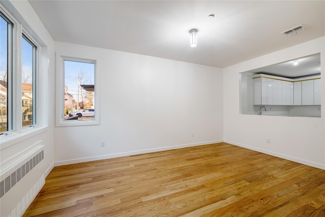 empty room featuring light wood-style floors, visible vents, baseboards, and radiator