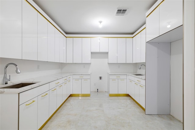 kitchen with visible vents, light stone countertops, white cabinetry, and a sink