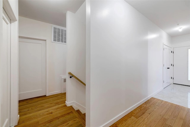 hallway featuring baseboards, an upstairs landing, visible vents, and light wood-type flooring