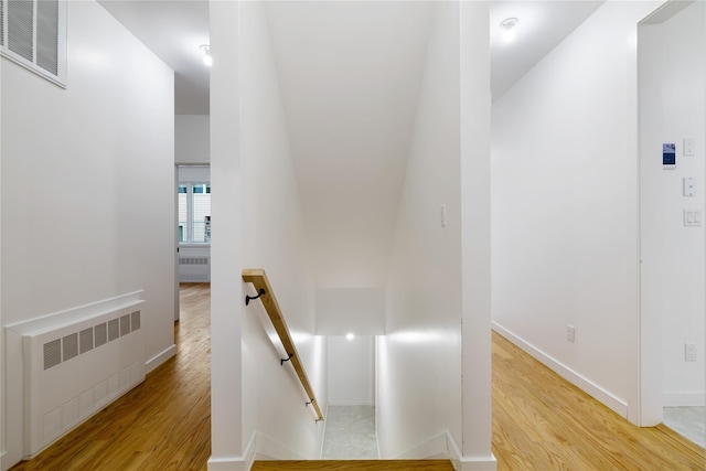 hallway with an upstairs landing, visible vents, radiator, and wood finished floors