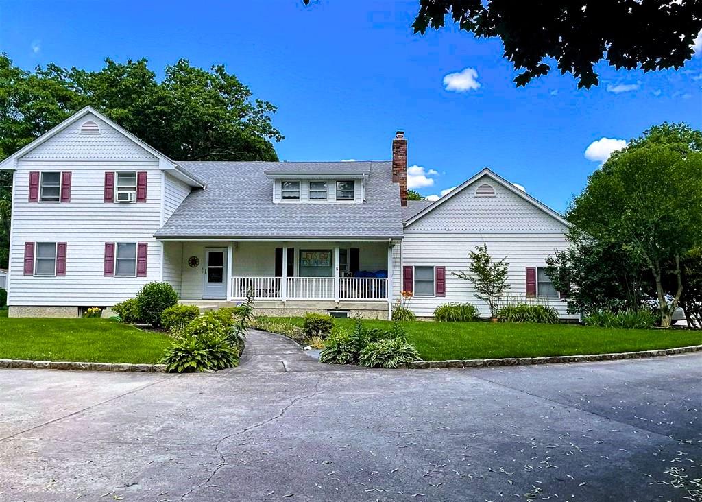 view of front of property featuring a porch, a front yard, a shingled roof, and a chimney