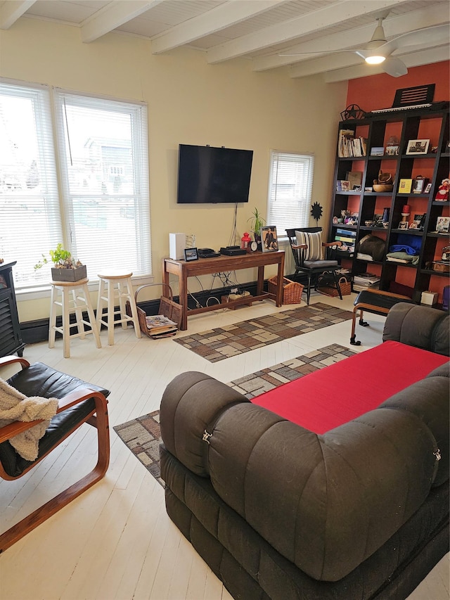 living area with beamed ceiling, plenty of natural light, wood-type flooring, and a ceiling fan