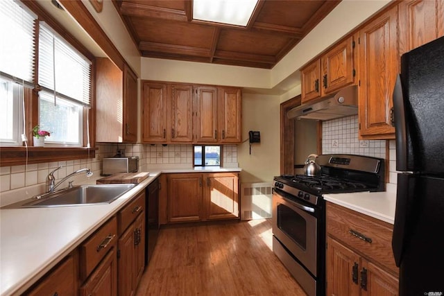 kitchen featuring brown cabinets, a sink, coffered ceiling, under cabinet range hood, and black appliances