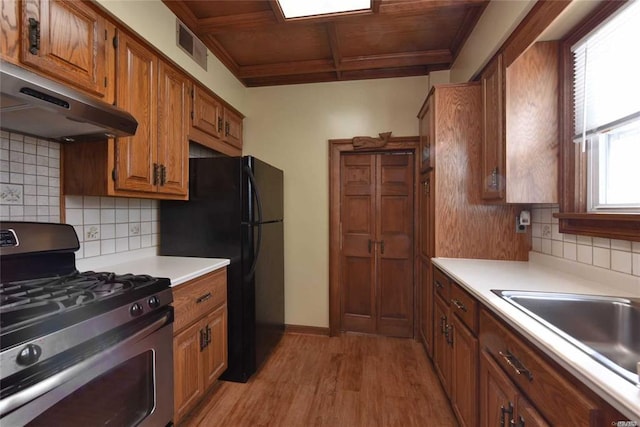 kitchen featuring light wood finished floors, freestanding refrigerator, stainless steel gas range, light countertops, and under cabinet range hood