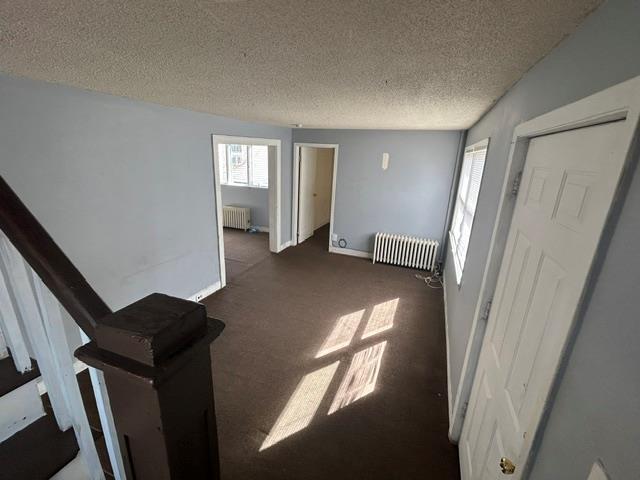 empty room with a textured ceiling, dark carpet, baseboards, and radiator