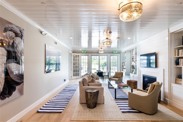 living room featuring built in shelves, wood finished floors, baseboards, ornamental molding, and a glass covered fireplace