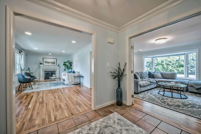 tiled living area featuring a glass covered fireplace, baseboards, ornamental molding, and recessed lighting