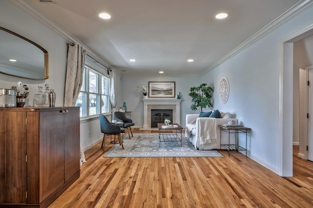 living area with baseboards, light wood-style floors, ornamental molding, and a tiled fireplace