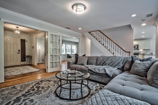 living area with visible vents, wood finished floors, stairs, and ornamental molding