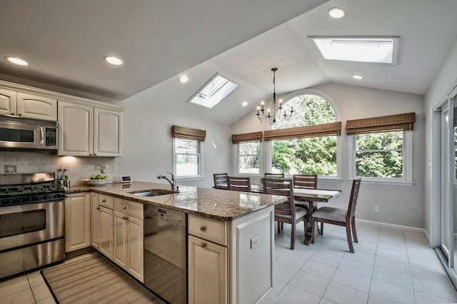 kitchen with a sink, stainless steel appliances, vaulted ceiling with skylight, a peninsula, and decorative backsplash