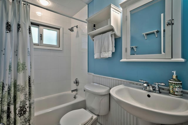 bathroom with wainscoting, toilet, shower / tub combo with curtain, and a sink