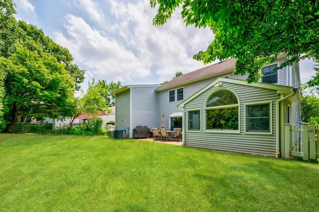 rear view of property featuring a yard, central air condition unit, fence, and a patio area