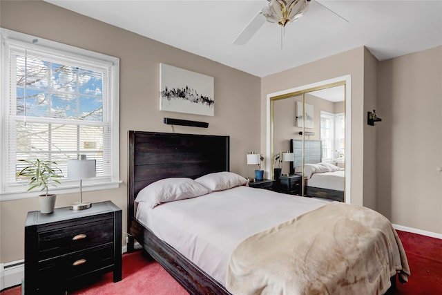 carpeted bedroom with a closet, baseboard heating, a ceiling fan, and baseboards