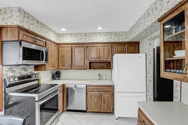 kitchen featuring wallpapered walls, light countertops, light tile patterned flooring, stainless steel appliances, and a sink